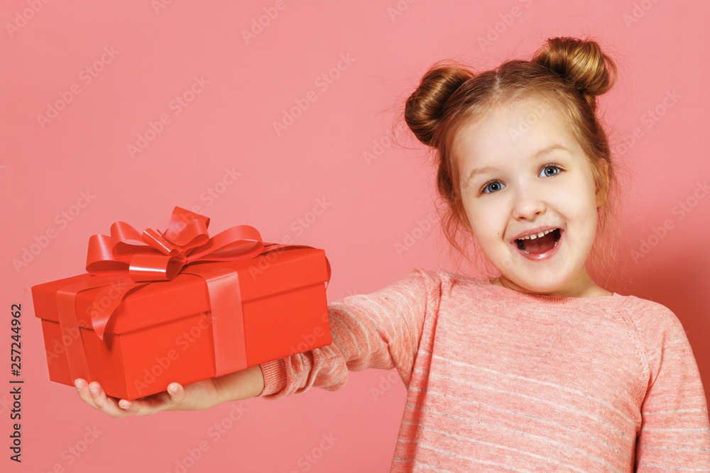 Closeup portrait of a cute little girl with hair buns on pink background. The child holds out a box with a gift. Closeup portrait of a cute little girl with hair buns on pink background. The child holds out a box with a gift.
