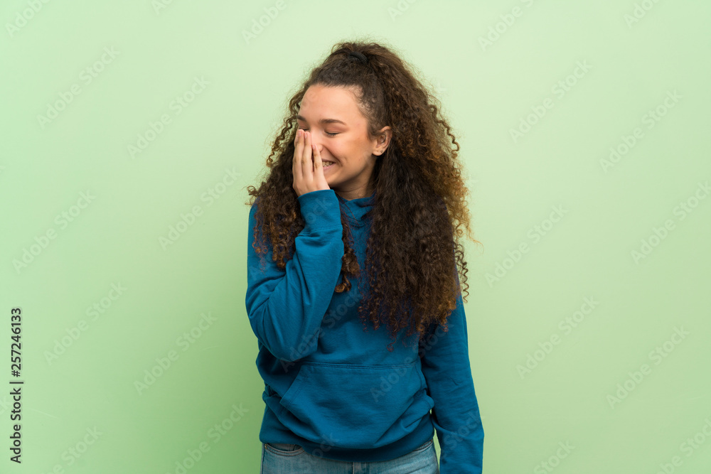 Teenager girl over green wall posing with arms at hip and laughing Teenager girl over green wall posing with arms at hip and laughing