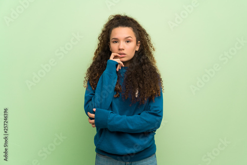 Teenager girl over green wall having doubts while looking up