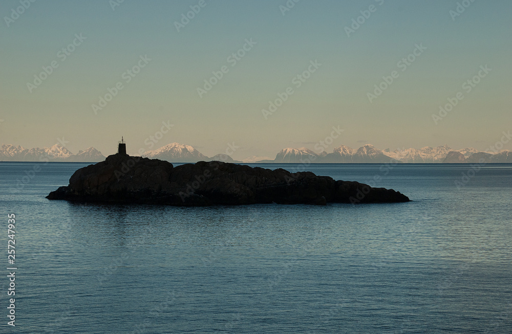 Silhouette of lighthouse on a reef in Lofoten, Norway, with snow covered mountains in the background. Silhouette of lighthouse on a reef in Lofoten, Norway, with snow covered mountains in the background.