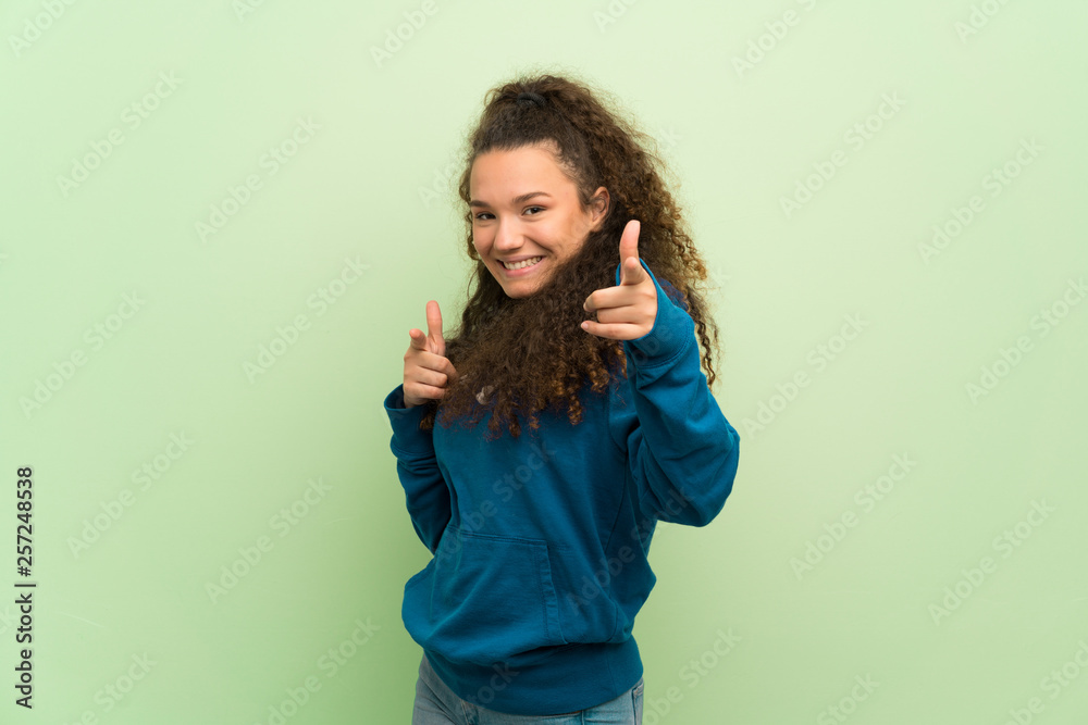 Teenager girl over green wall pointing to the front and smiling Teenager girl over green wall pointing to the front and smiling