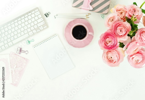 Flat lay top view women's office desk . Female workspace with laptop, pink flowers ranunkulus, accessories, notebooks, glasses, cup of coffee on white background. Copy space. 