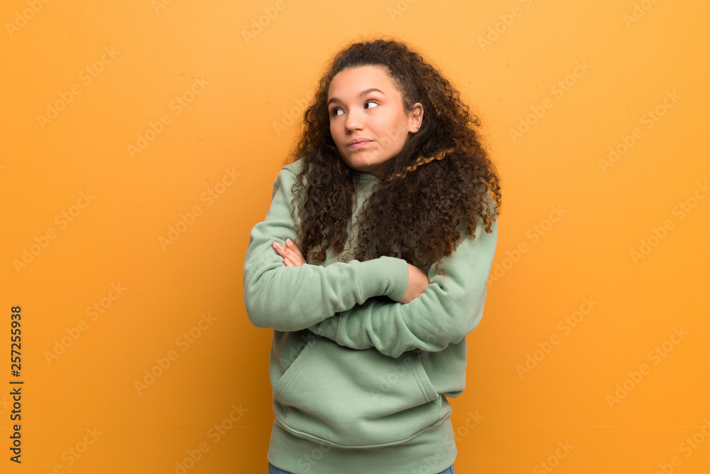 Teenager girl over ocher wall making doubts gesture while lifting the shoulders Teenager girl over ocher wall making doubts gesture while lifting the shoulders