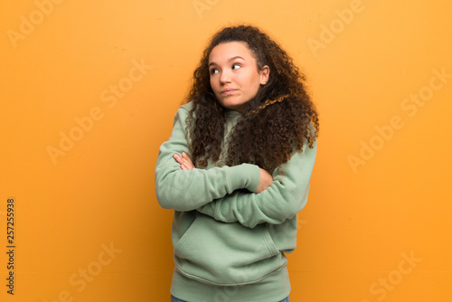 Teenager girl over ocher wall making doubts gesture while lifting the shoulders © luismolinero