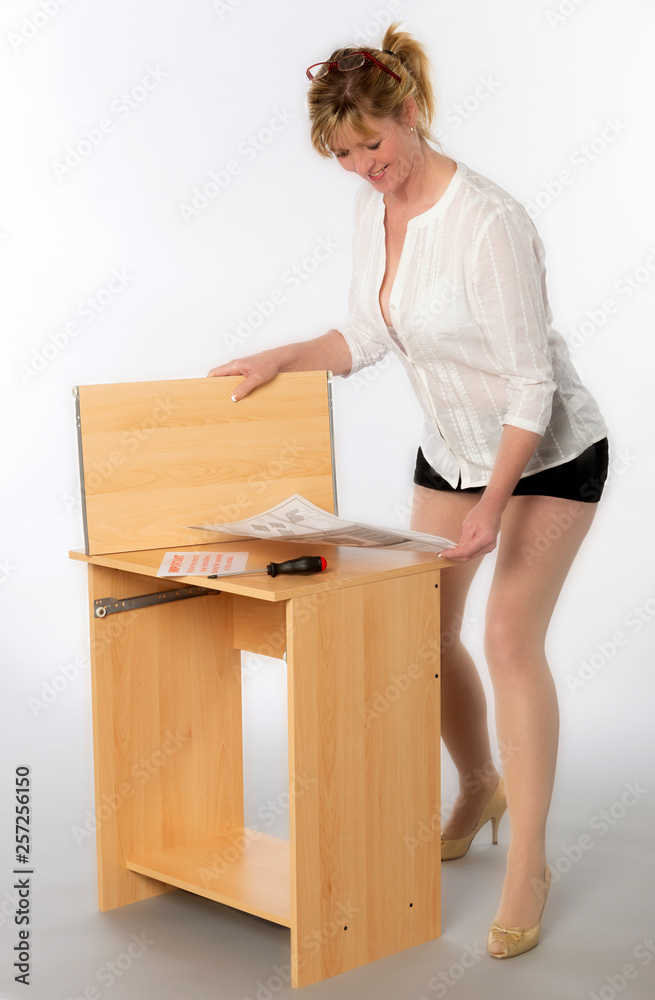 Woman constructing a personal computer desk from a flatpack, Using the instructions and a screwdriver Woman constructing a personal computer desk from a flatpack, Using the instructions and a screwdriver