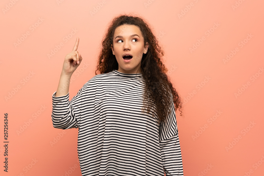 Teenager girl over pink wall intending to realizes the solution while lifting a finger up Teenager girl over pink wall intending to realizes the solution while lifting a finger up