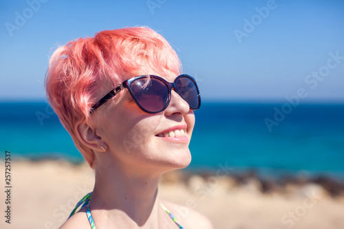 Young female model with pink hair and sunglasses on the beach