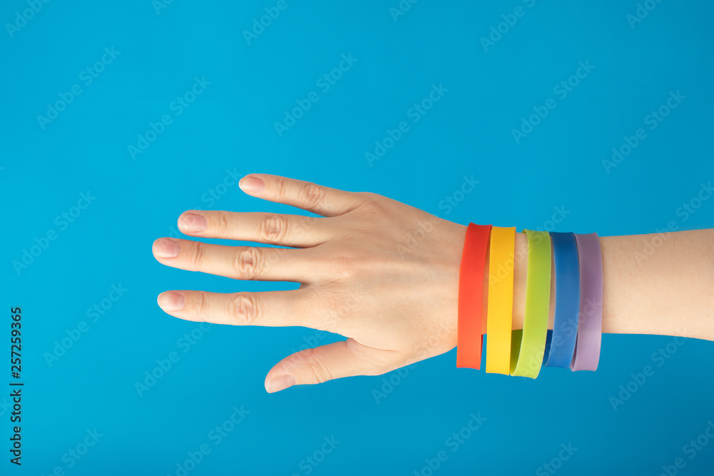 Rainbow flag LGBT wristband bracelet on female hand on blue background. Gay pride concept. Vote for homosexual love.