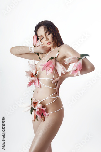 Beautiful naked woman girl tied with ropes and Lily flowers. Art spring summer fashion woman, perfect body, portrait of girl on white isolate background. Sexy brunette with pink lilies