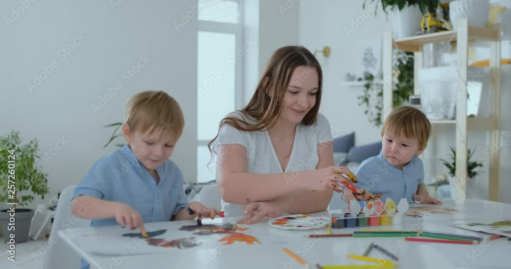 The family has fun painting on paper with their fingers in paint. Mom and two children paint with fingers on paper The family has fun painting on paper with their fingers in paint. Mom and two children paint with fingers on paper