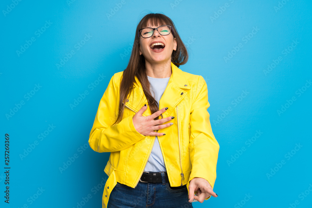 Young woman with yellow jacket on blue background smiling a lot while putting hands on chest Young woman with yellow jacket on blue background smiling a lot while putting hands on chest