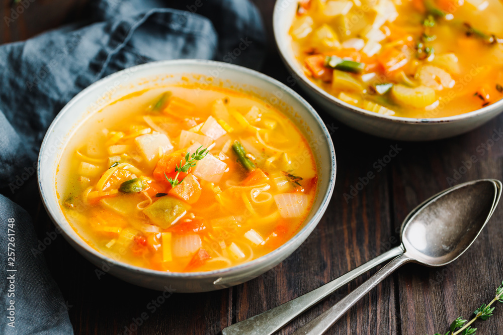 Spring vegetable soup with chicken stock for one person on wooden table. Rustic style, close-up view. Spring vegetable soup with chicken stock for one person on wooden table. Rustic style, close-up view.
