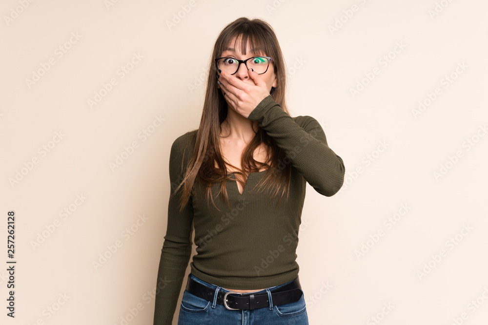 Young woman on ocher background covering mouth with hands Young woman on ocher background covering mouth with hands