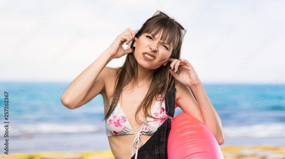 Young woman in bikini frustrated and covering ears at the beach