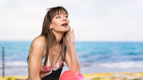 Young woman in bikini listening to something by putting hand on the ear at the beach