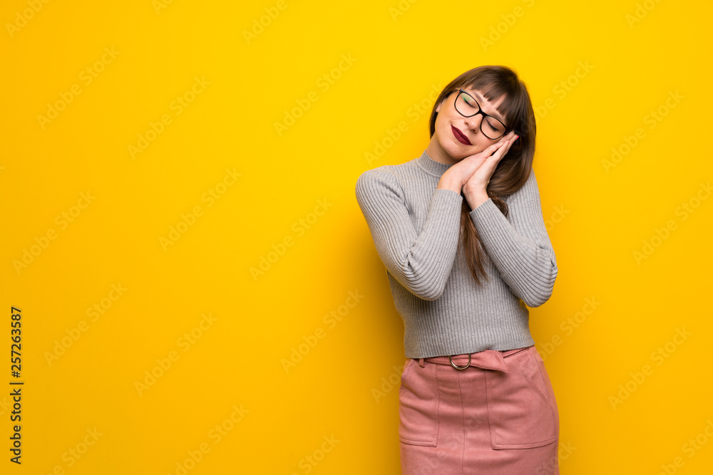 Woman with glasses over yellow wall making sleep gesture in dorable expression Woman with glasses over yellow wall making sleep gesture in dorable expression