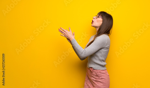 Woman with glasses over yellow wall applauding after presentation in a conference