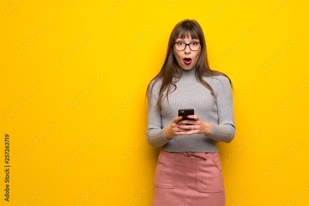 Woman with glasses over yellow wall surprised and sending a message Woman with glasses over yellow wall surprised and sending a message