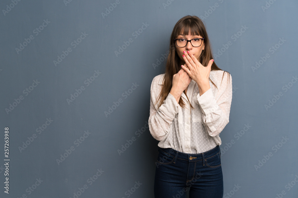 Woman with glasses over blue wall covering mouth with hands for saying something inappropriate Woman with glasses over blue wall covering mouth with hands for saying something inappropriate