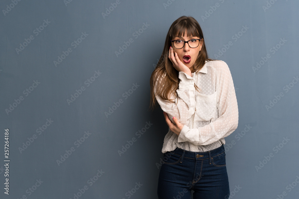 Woman with glasses over blue wall surprised and shocked while looking right Woman with glasses over blue wall surprised and shocked while looking right