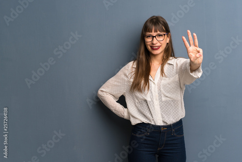 Woman with glasses over blue wall happy and counting three with fingers