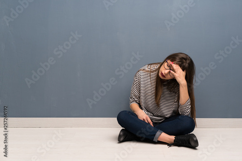 Woman with glasses sitting on the floor with tired and sick expression