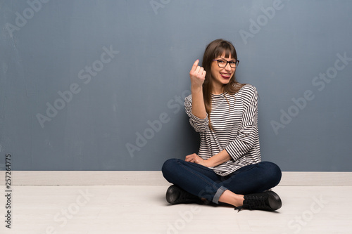 Woman with glasses sitting on the floor making money gesture