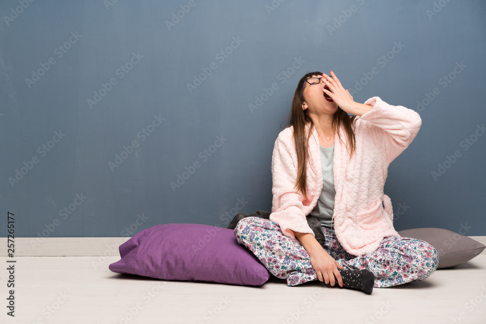 Woman in pajamas on the floor yawning and covering wide open mouth with hand Woman in pajamas on the floor yawning and covering wide open mouth with hand