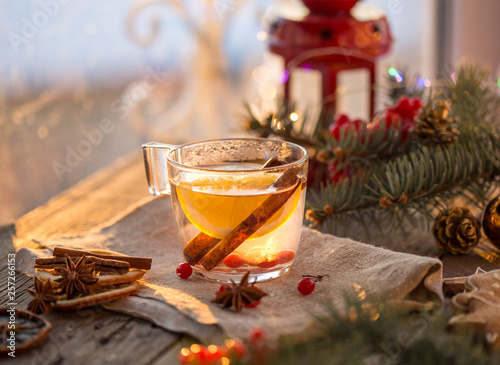 Winter theme. Christmas tea with spices, cup of tea with orange, cinnamon, anise, cookies in a shape of star, pepper and gray scarf on wooden background. Flat lay, View from above. Copy space for text