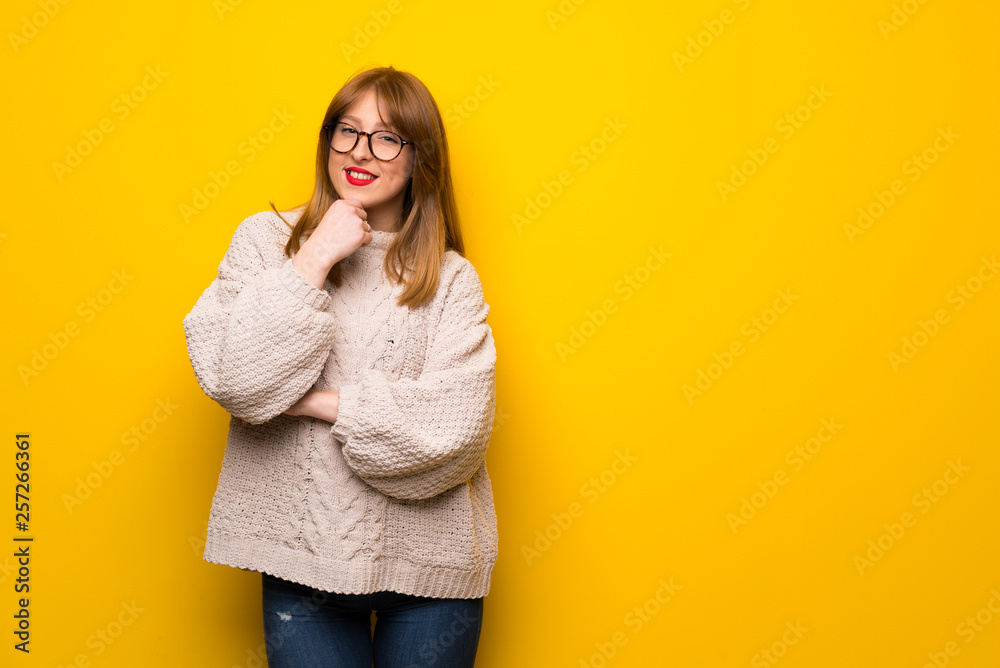 Redhead woman over yellow wall with glasses and smiling Redhead woman over yellow wall with glasses and smiling