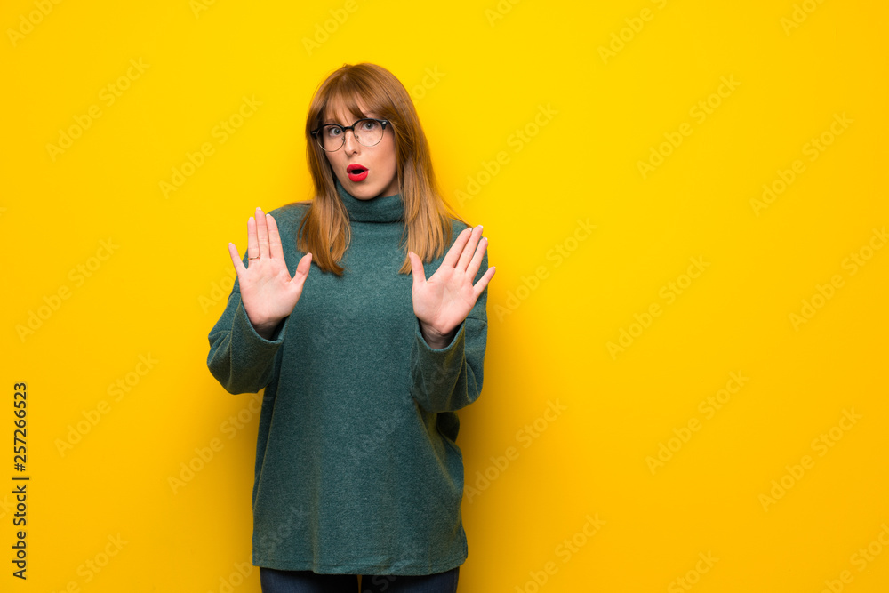 Woman with glasses over yellow wall making stop gesture with both hands - obrazy, fototapety, plakaty 