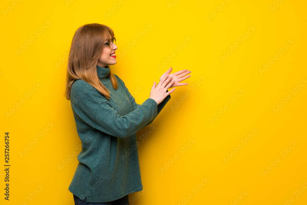 Woman with glasses over yellow wall applauding after presentation in a conference Woman with glasses over yellow wall applauding after presentation in a conference