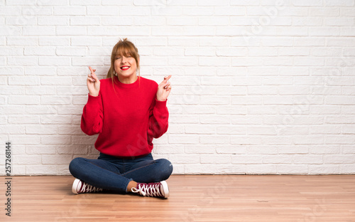 Redhead woman siting on the floor with fingers crossing and wishing the best