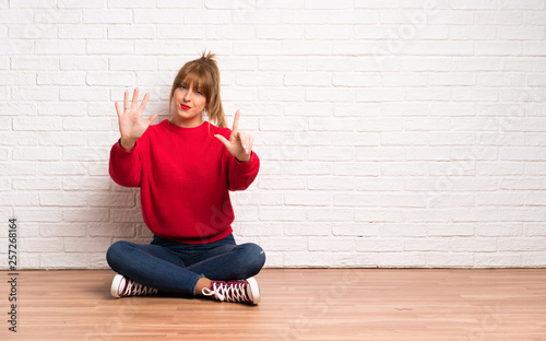 Redhead woman siting on the floor counting seven with fingers