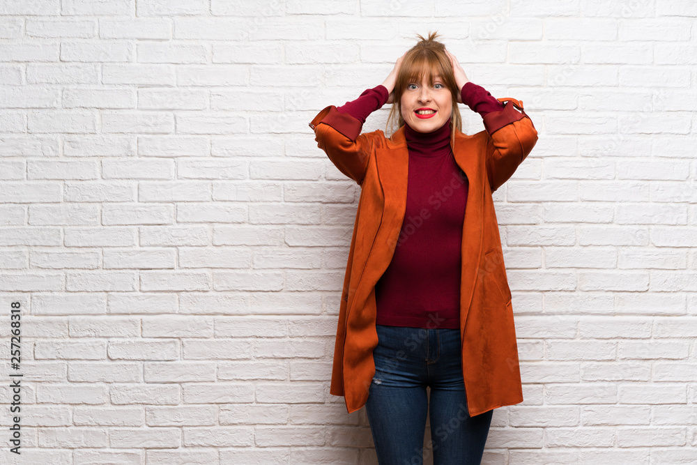 Woman with coat over white brick wall frustrated and takes hands on head Woman with coat over white brick wall frustrated and takes hands on head