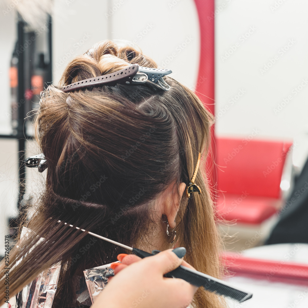 Fototapeta premium Young professional hairdresser applying dye on clients hair
