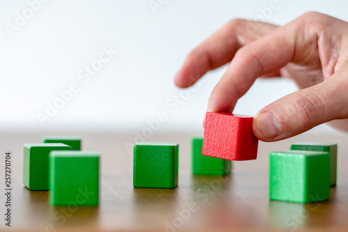 human hand picking up a red wooden cube out of a group of some green cubes