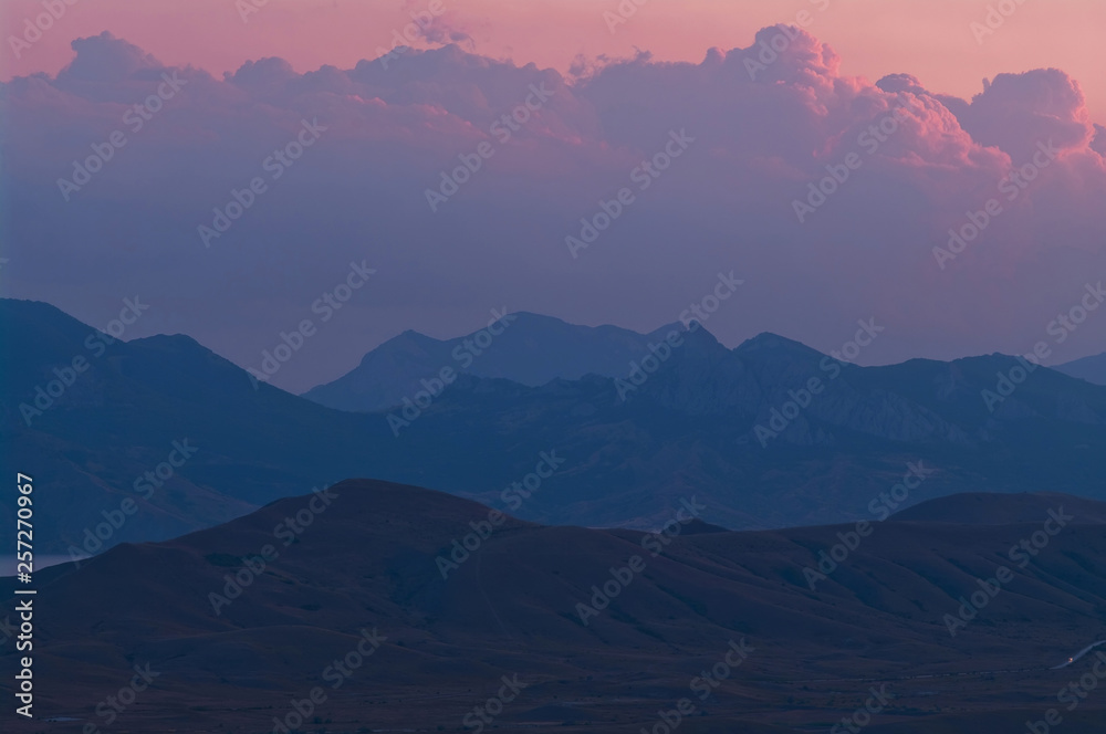 Purple sunset in the mountains. Evening landscape in a hilly area with purple clouds.