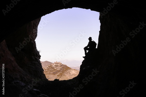 ADVENTURER SITTING AT THE ENTRANCE OF A CAVE LOOKING AT A CASTLE