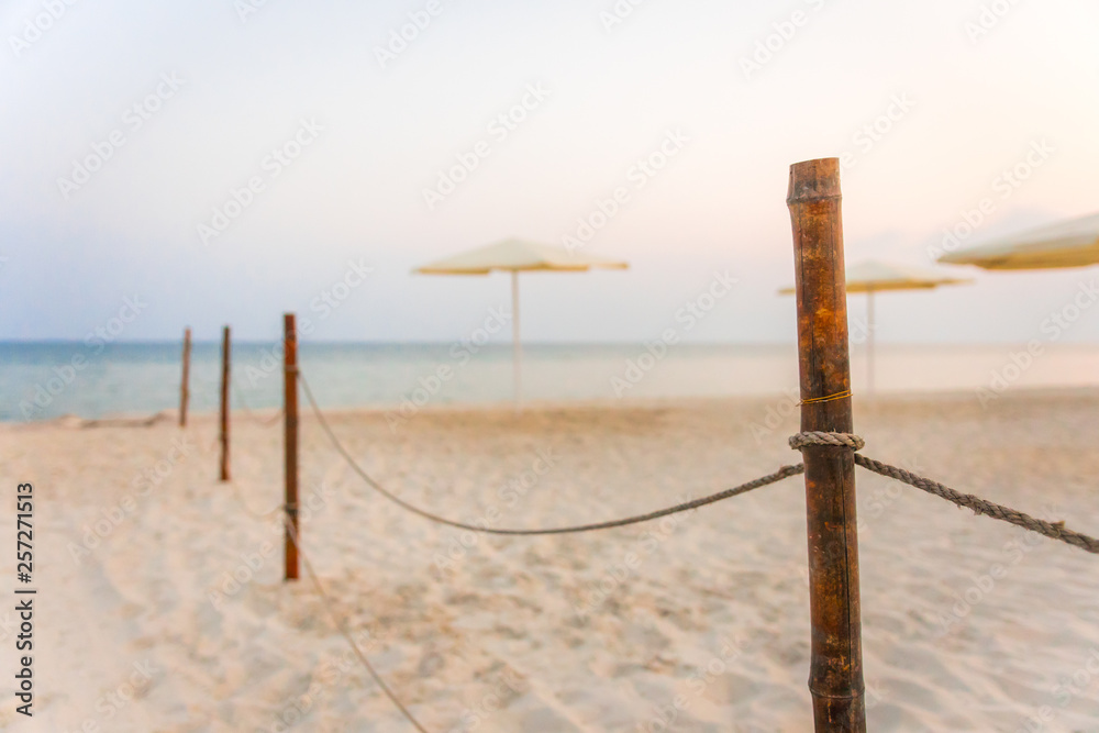 Rope fence on the sandy beach, white beach umbrellas. Sunset on the beach.