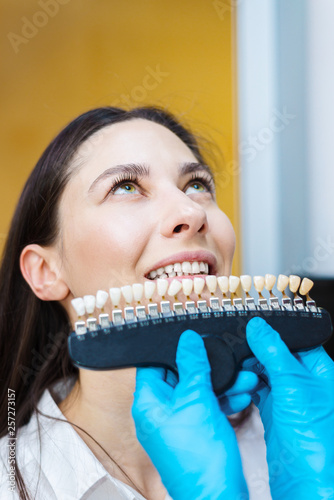 dentist checks teeth. Doctor holds color samples for teeth whitening. oral hygiene concept.