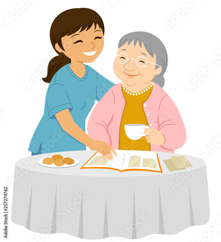 Young female caregiver smiling to an elderly woman who is placing photos in an album