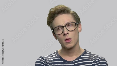 Portrait of thoughtful teenager in eyeglasses. Smart caucasian nerd boy in glasses with thoughtful expression agaist gray background. Young man has an idea. photo