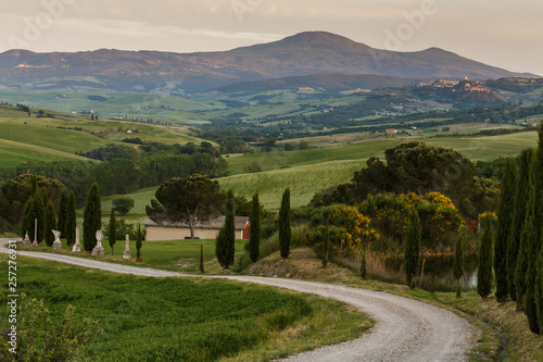 Typical Tuscany landscape after sunset with the twisting road, cypress trees, hills and meadows, village houses. Travel Italy.