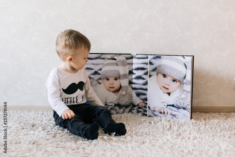 Naklejka premium Cute baby sitting on the background of a large stylish photo book with your photos