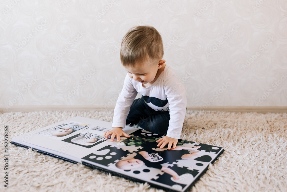 Cute baby sitting and looking at a large stylish photo book with their photos. Children's photo album