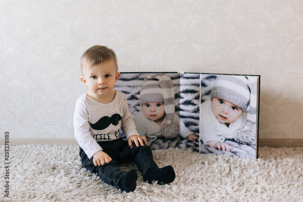 Naklejka premium Cute baby sitting on the background of a large stylish photo book with your photos