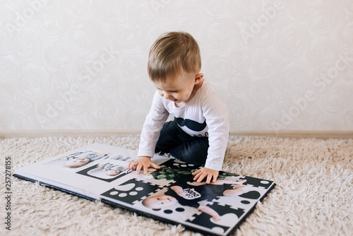 Obraz na płótnie Cute baby sitting and looking at a large stylish photo book with their photos. Children's photo album w salonie
