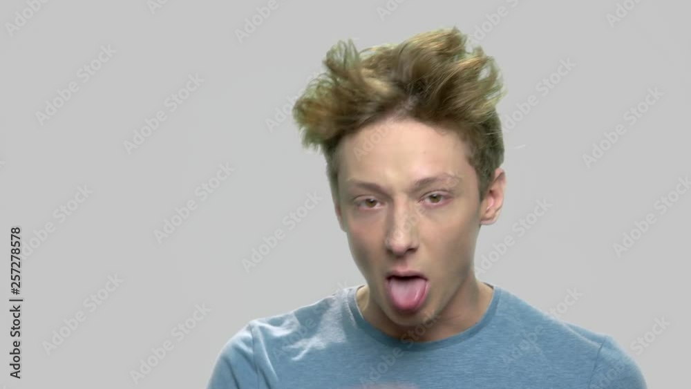 Rude teen boy making face grimace. Teenage boy sticking his tongue out against gray background. Adolescent guy teasing at camera. Rude teen boy making face grimace. Teenage boy sticking his tongue out against gray background. Adolescent guy teasing at camera.