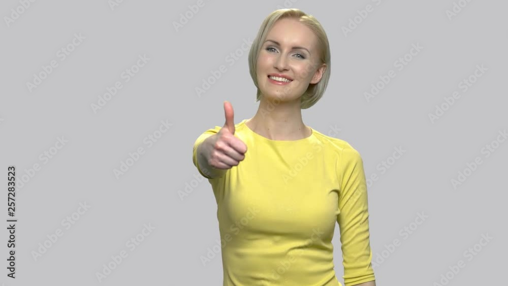Pretty caucasian woman giving thumb up sign. Charming middle-aged blonde woman gesturing thumb up against gray background. People, gestures and emotions. Pretty caucasian woman giving thumb up sign. Charming middle-aged blonde woman gesturing thumb up against gray background. People, gestures and emotions.